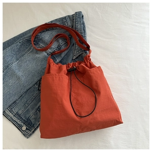 Detail of orange drawstring tote bag featuring side pockets and nylon texture close-up