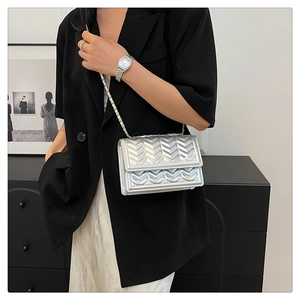 Close-up of a silver quilted small square bag with woven metal chain strap on a black blazer