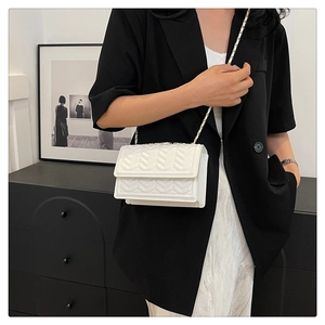 Detail of white crossbody bag featuring V-shaped quilting and a leather chain strap