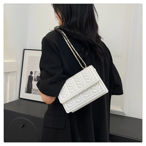 Close-up of white V-quilted shoulder bag with elegant metal chain strap and flap closure