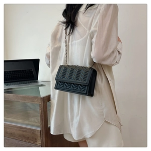 Detail of a black quilted crossbody bag with golden chain strap on a female model