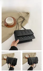 Detail of a black chevron quilted shoulder bag with gold chain strap on lifestyle background