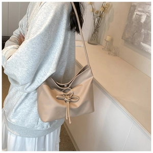 Detail of soft beige PU leather bucket bag featuring a decorative string bow and pleats