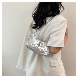 Detail of silver quilted shoulder bag featuring metal star logo and chain strap on model