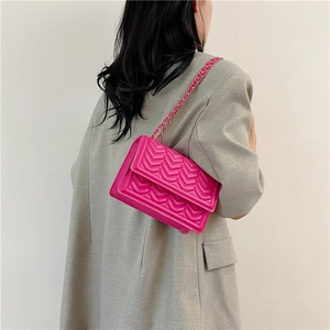 Minimalist fuchsia quilted chain crossbody bag shown on a model with a grey blazer coat