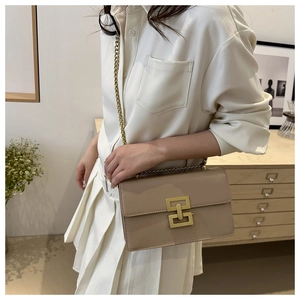 Detail of khaki chain strap shoulder bag with gold geometric buckle in home setting