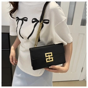 Minimalist black leather crossbody bag with a golden chain strap and geometric buckle