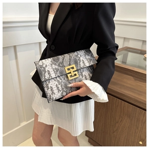 Détail de la pochette enveloppe à motif serpent avec boucle dorée portée par un mannequin