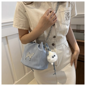 Detail of light blue bucket bag with silver butterfly charm and plush pompom pendant