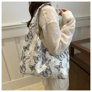 Detail of white textured fabric shoulder bag with black butterfly prints worn by model