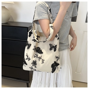 Detail of black butterfly embroidery on a white canvas tote bag worn by a model
