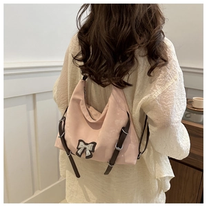 Détail du sac à bandoulière rose en nylon avec sangle en cuir marron et nœud argenté