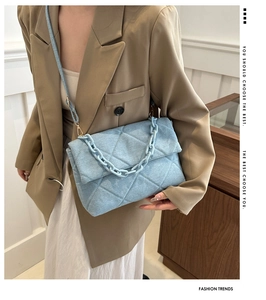 Close-up of quilted denim shoulder bag with chunky blue chain handle and beige suit detail