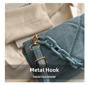 Macro shot of blue denim bag featuring gold metal hooks and a light blue chain strap