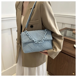 Detail of light blue quilted denim shoulder bag with chic resin chain and flap closure