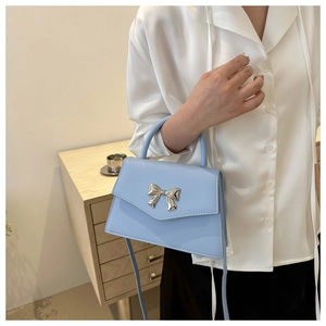 Close-up of a light blue square handbag featuring a silver metal bow and leather handle