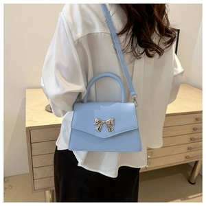 Detail of light blue handbag with silver bow ornament worn by model in a home setting