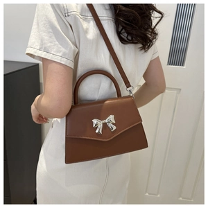 Detail of a brown leather crossbody bag with silver bow ornament worn by a model