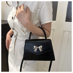 Close-up of black square handbag featuring a silver metal bow accent and polished finish