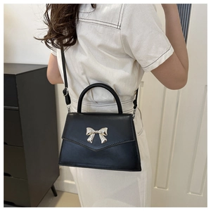 Detail of black crossbody bag with silver bow accent worn by a model in a white dress