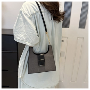 Detail of grey crossbody bag with black strap, gold chain, and matte square buckle