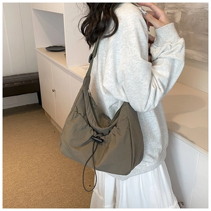 Side view of olive green crescent nylon tote bag shown on model in minimal interior