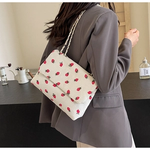 Detailed shot of white corduroy shoulder bag with red strawberry embroidery and chain strap