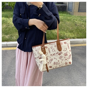 Detailed view of cream graffiti tote bag with brown leather handles and rabbit charm