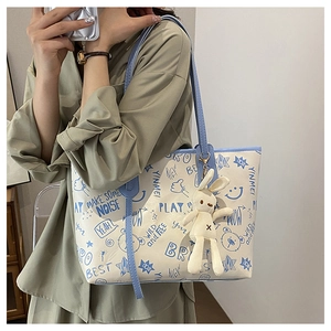 Detail of graffiti print tote bag with plush rabbit charm worn by a model