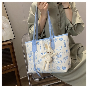 Detail of printed tote bag with blue trim, graffiti patterns and cute bunny charm accessory