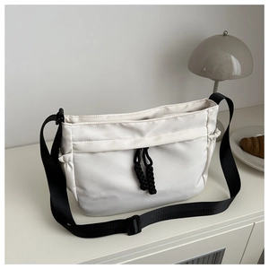 Detail van witte nylon schoudertas met zwart trekkoord en brede verstelbare draagriem