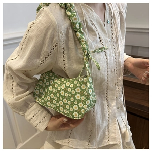 Detail of floral underarm bag with ruffled strap and daisy print on green fabric
