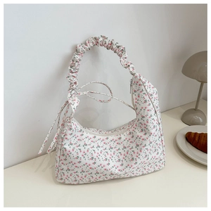 Detail of floral crescent shoulder bag featuring ruched strap and side ribbon accents