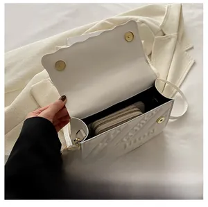 Detail view of white leather crossbody bag with letter embossing and magnetic clasp