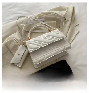 Detail of white quilted crossbody bag with FASHION embossing and woven handle