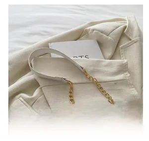 Detail eines Schultergurts aus weißem Leder und Goldkette auf einem cremefarbenen Blazer