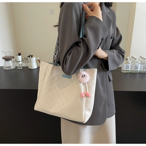 Detail of checkered tote bag with blue logo patch and pink plush charm accessory