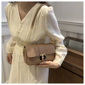 Detail of light brown crocodile pattern flap bag with gold chain strap on model