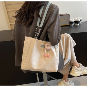 Detail of cream plaid tote bag with light blue leather strap and plush monster charm