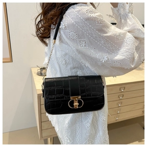Detail of black faux crocodile skin bag with golden T-shaped lock and chain strap