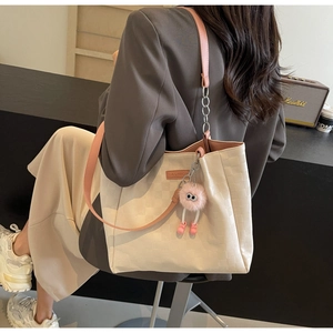 Detail of cream checkered tote bag with pink straps and plush monster charm decoration