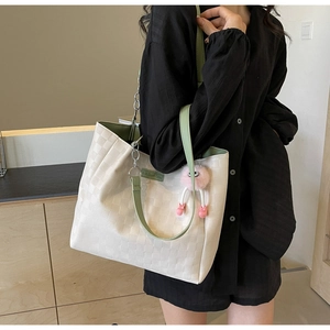Detail of checkered cream tote bag featuring green leather straps and a plush charm
