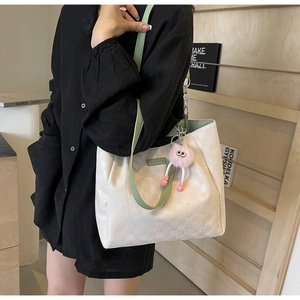 Detail of checkered tote bag with green straps and pink plush pendant on model