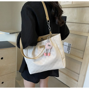 Detail of white checkered tote bag with pink plush monster charm and silver chain strap