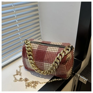 Détail du sac cylindrique à carreaux rouges avec chaîne dorée et tissu en laine