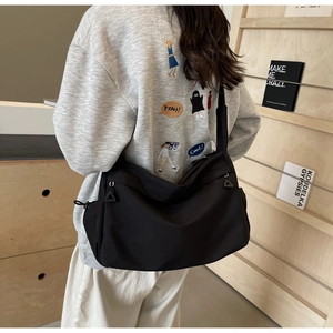 Rear view of a black nylon crossbody bag worn on person against a library background