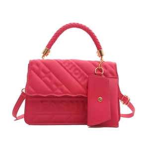 Fashionable magenta crossbody bag with embossed lettering and woven handle on white background