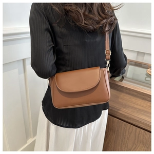 Elegant brown leather crossbody bag with gold hardware shown on a model in a bright room