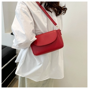 Detail of red faux leather shoulder bag with gold metal buckle and elegant flap design