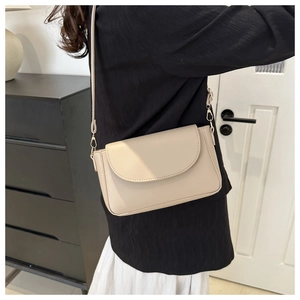 Close-up of beige minimalist crossbody bag with gold lobster clasp and curved flap detail